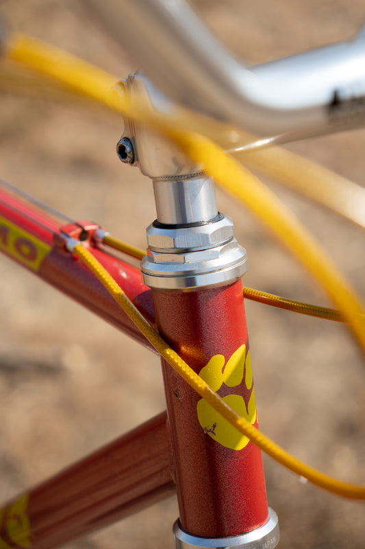Close-up of a bicycle frame with a red top tube, yellow graphics, and a silver headset, with yellow cables running through the frame.